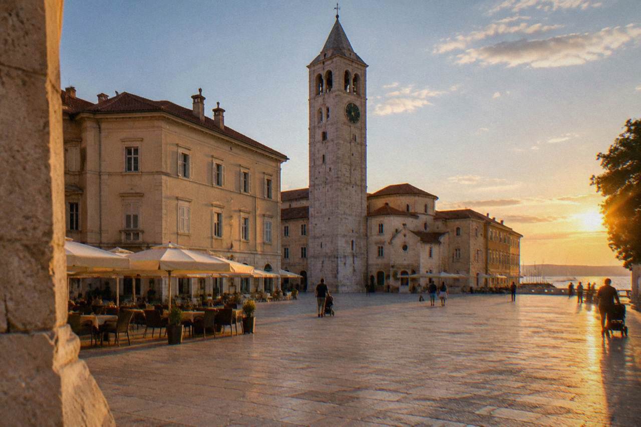 Stone square with a clock tower, cafe parasols and pale buildings