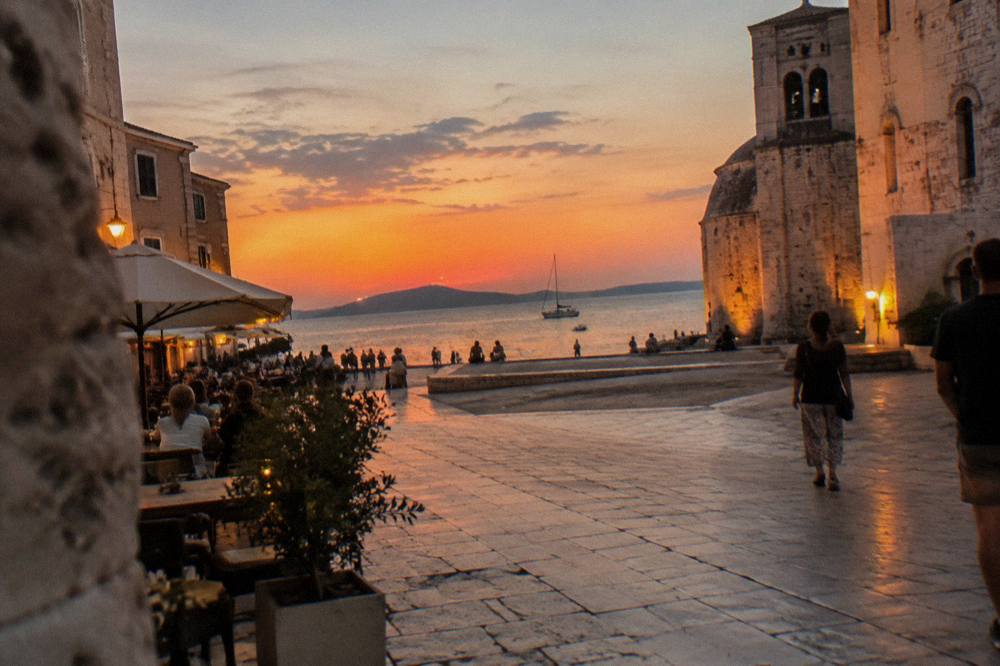 Square at evening with lamplight on pale walls and cafe tables