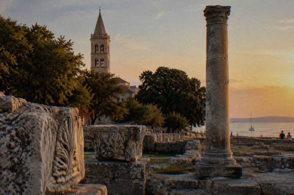 Weathered forum stones and a tall column with a bell tower beyond