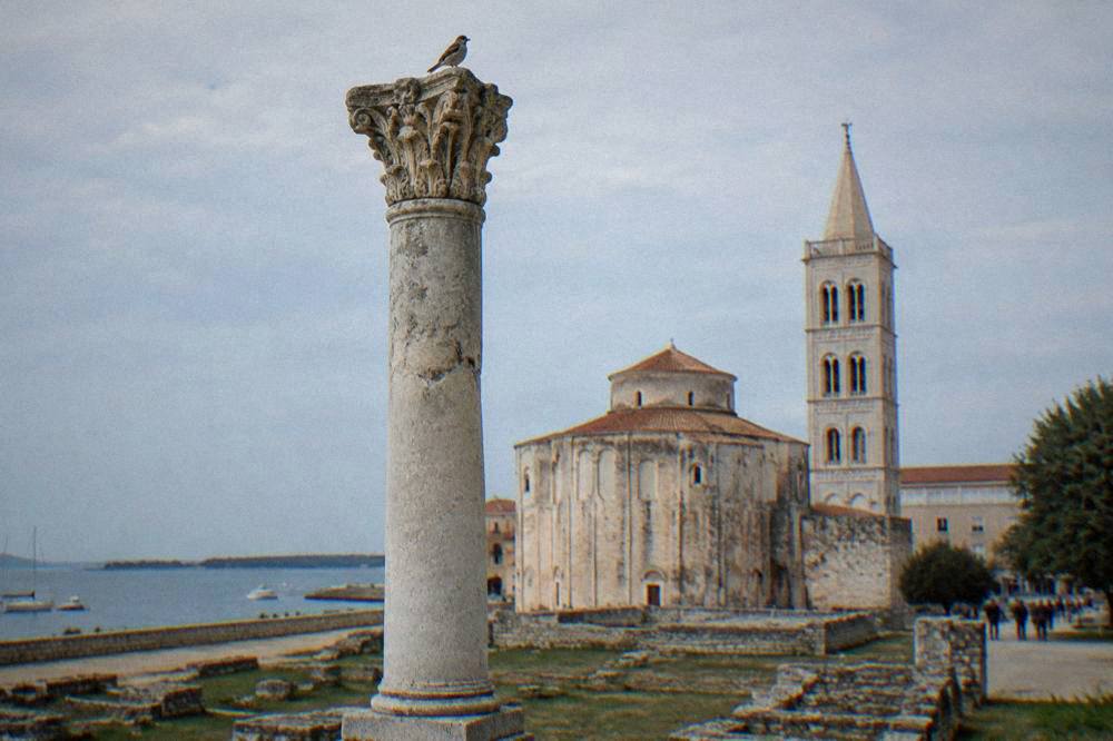 Single Roman column against pale blue sky with a bell tower behind