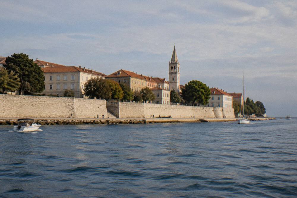 Riva and city wall seen from the water with a bell tower behind