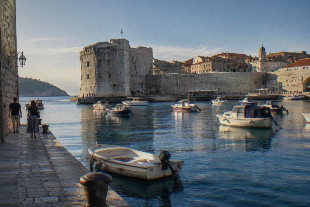 Dubrovnik old harbour with small boats and fortress walls in summer light