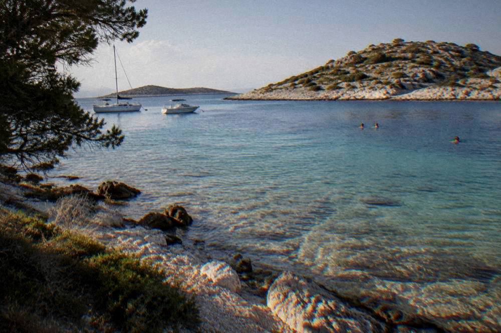 Small Kornati cove with clear shallow water and distant swimmers