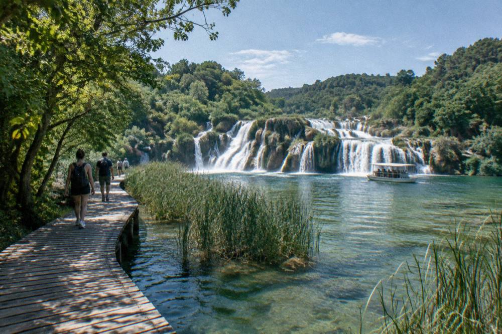 Wooden boardwalk over green water and small travertine falls at Krka