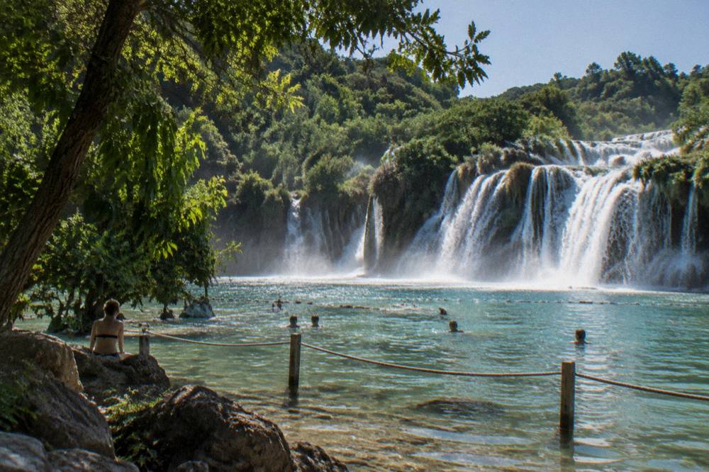 Turquoise swimming pool at the base of a waterfall with distant swimmers