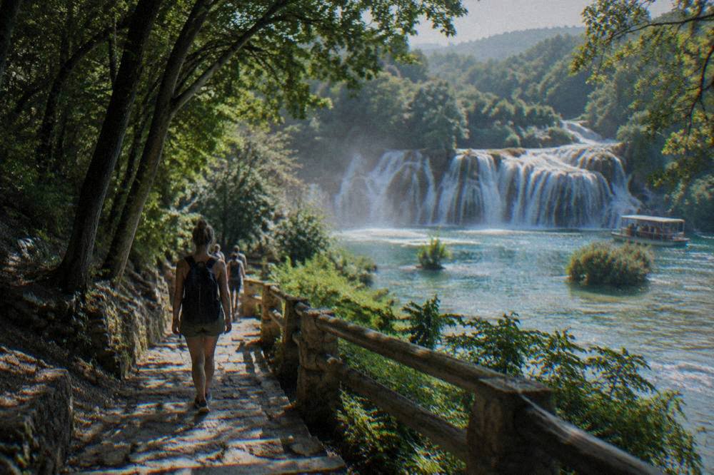 Shaded forest path to the falls with a backpacker seen from behind