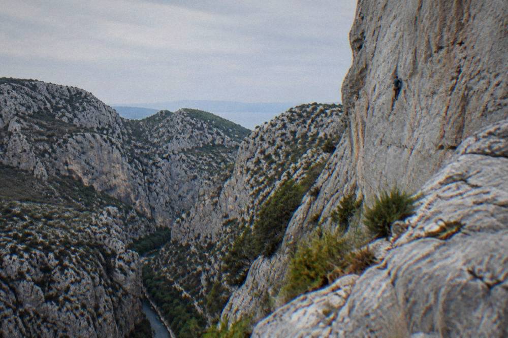 Distant climber on a pale limestone wall above the canyon