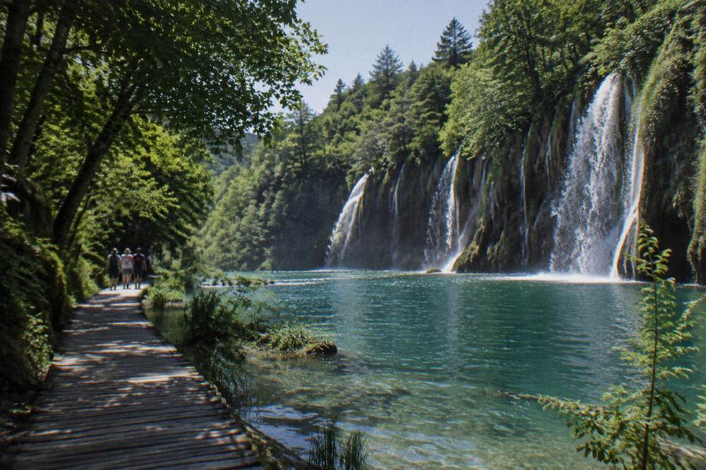 Small distant group walking a wooden boardwalk beside a waterfall