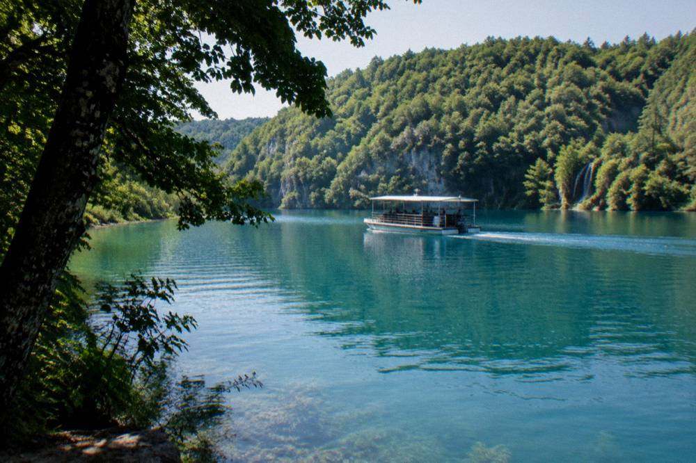 Boat gliding across a calm turquoise lake with forested shores