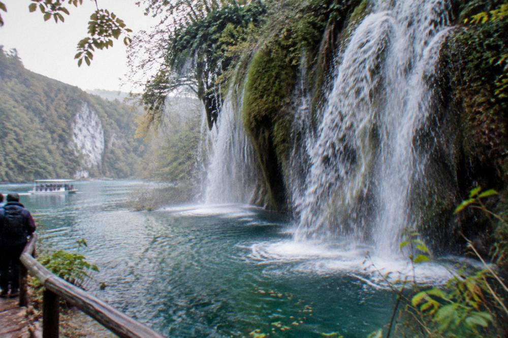 Waterfall pouring over mossy travertine into a deep turquoise pool