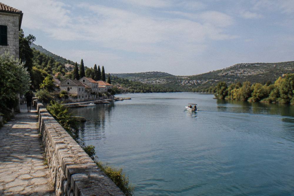 Calm river estuary near Skradin with tree-lined banks and a lone boat