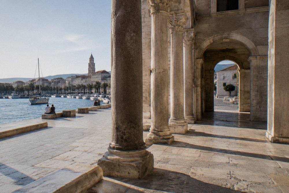 Roman stone courtyard with tall columns and an arched passage