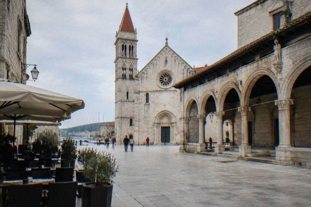 Trogir main square with a pale loggia, cathedral facade and cafe tables