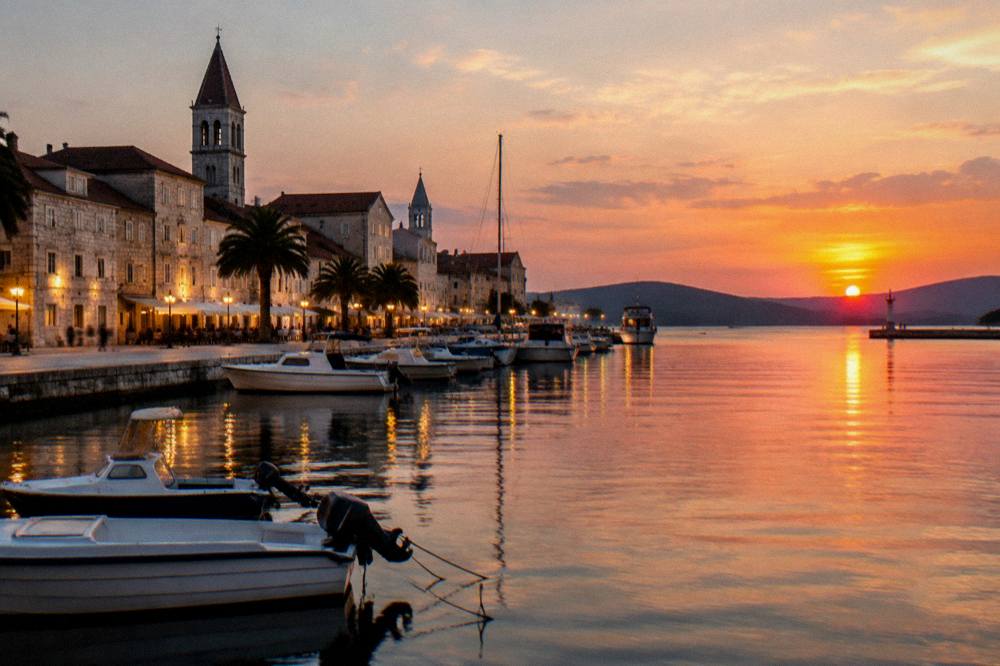 Trogir waterfront at dusk with lit facades reflected on still water