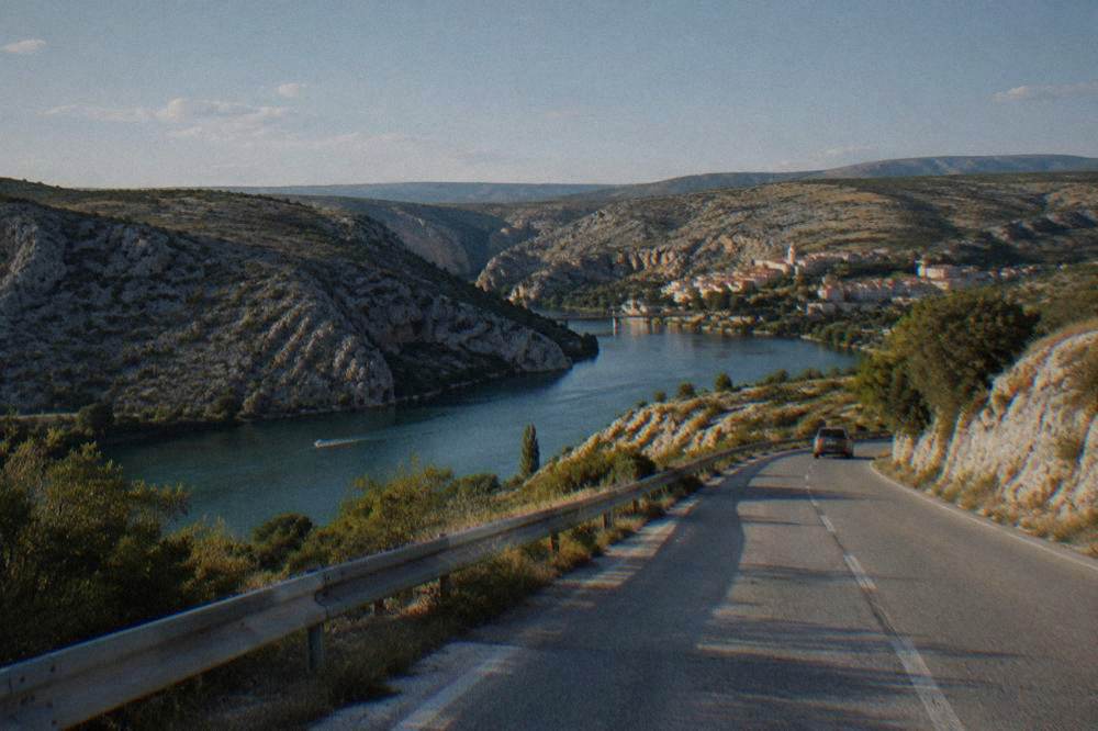 Road toward Obrovac across rocky karst hills with scrub in summer light
