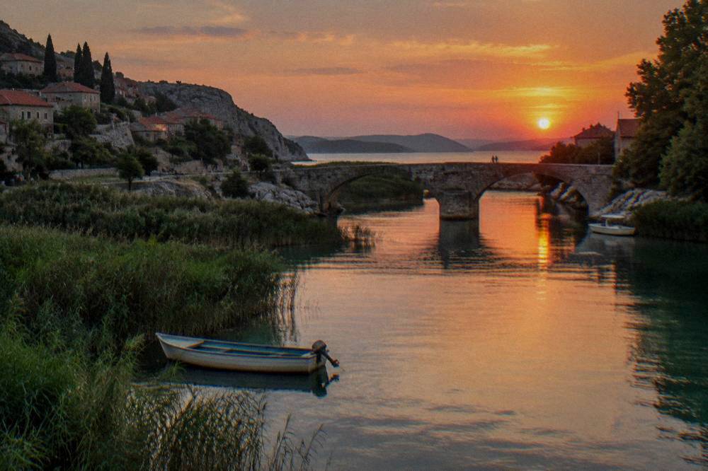 Calm lower river with reeds and a stone bridge at Obrovac