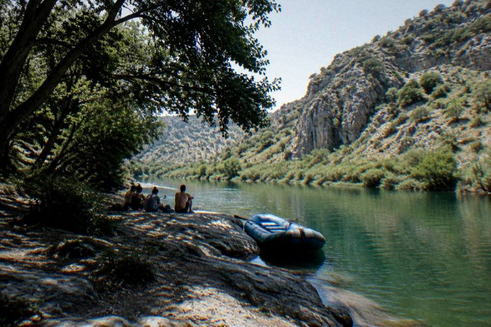 Paddlers resting on a flat rock beside a calm green stretch of river