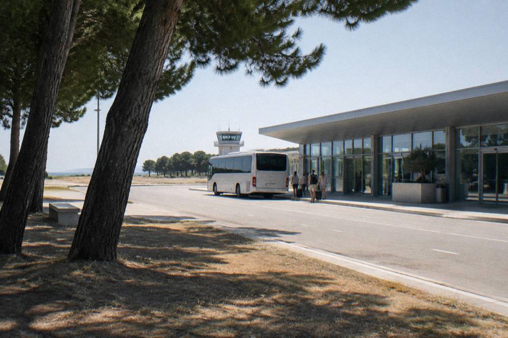 A small airport terminal with a shuttle bus waiting at the kerb under a clear sky.
