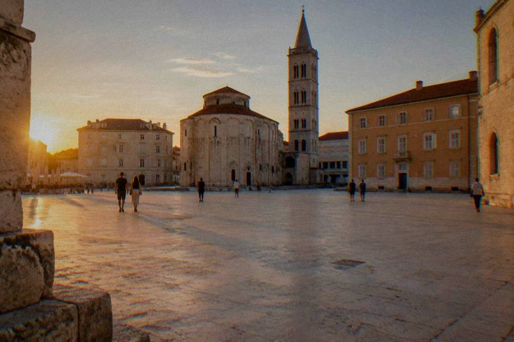 Distant people strolling across pale paving in an Old Town square in late afternoon light.