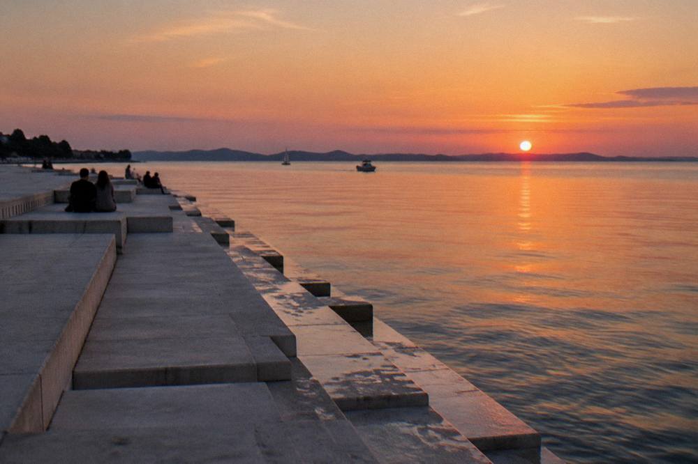 The white stone steps of the Sea Organ meeting the water at dusk with a few distant sitters.