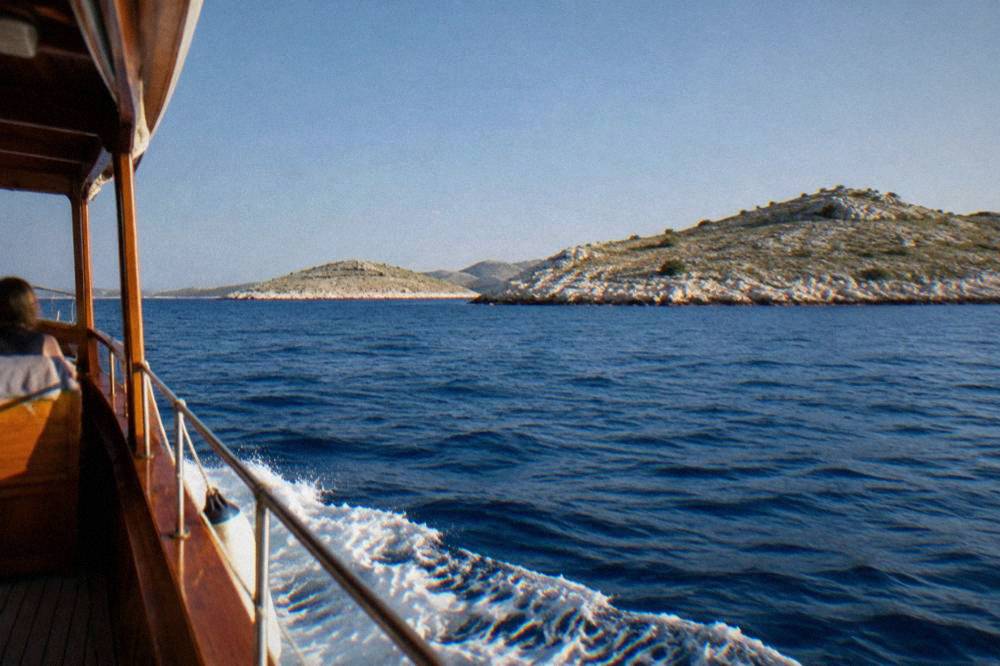 A wooden boat passing low bare Kornati islands on clear blue water in summer.