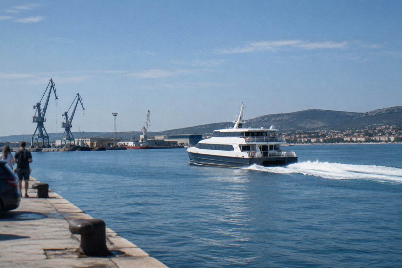 A fast passenger catamaran leaving a Croatian quay with a white wake on calm water.