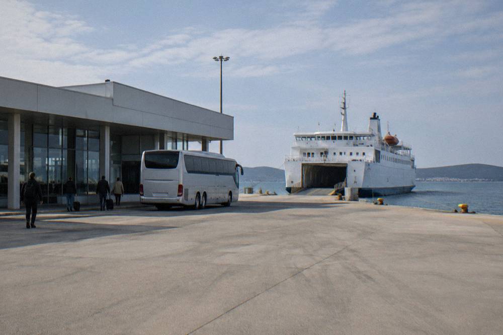 A modern ferry terminal building with a bus waiting beside it and a ferry moored behind.