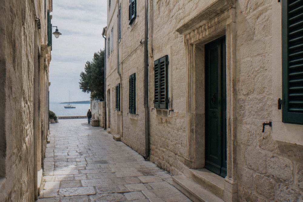A car-free pale stone lane in Zadar Old Town with cream walls and green shutters.