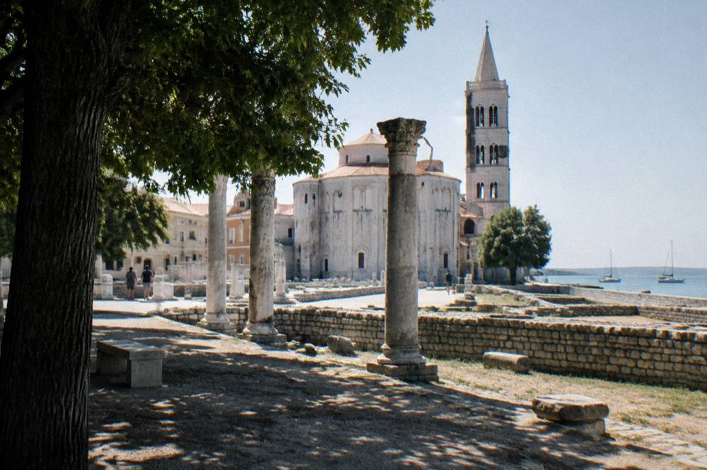 Weathered Roman columns and ruins of the forum beside a pale stone church in Zadar.