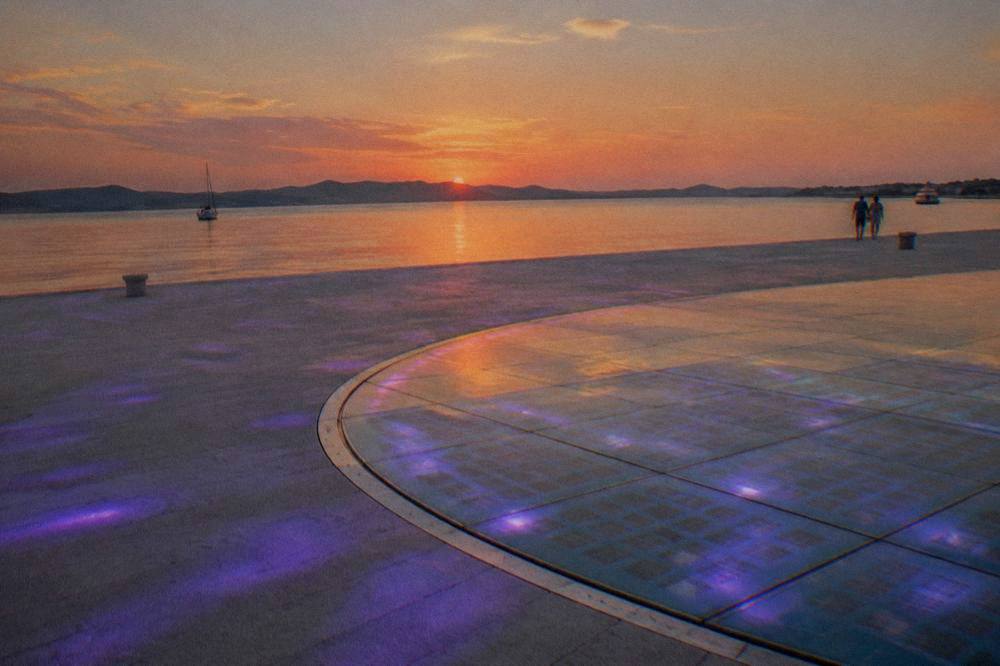 The glass circle of the Greeting to the Sun glowing at dusk on the waterfront.