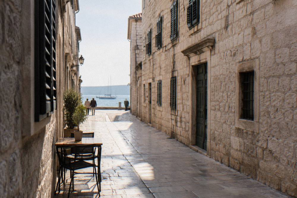 A narrow cream-stone lane in Zadar Old Town with shuttered windows and an empty cafe table.