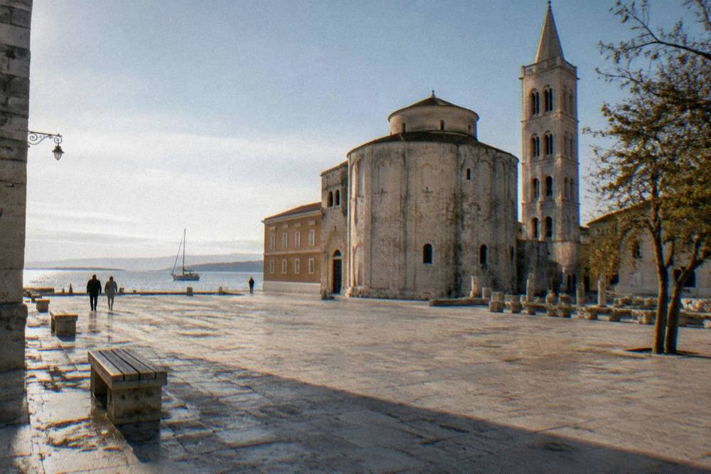 A pale stone Old Town square in mild light with long shadows and empty benches.
