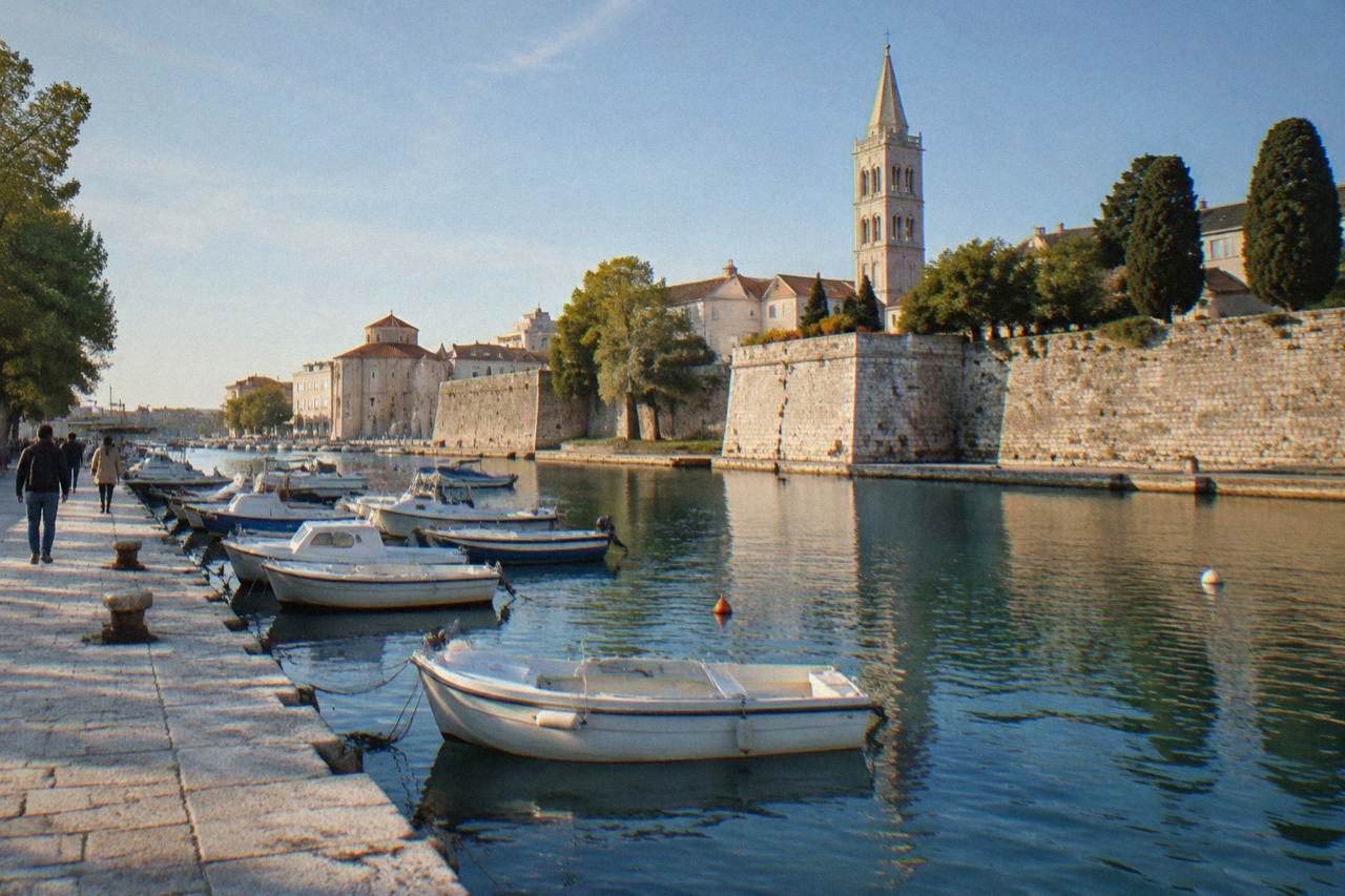 Small boats moored along Zadar's waterfront with the Old Town walls and bell tower behind.