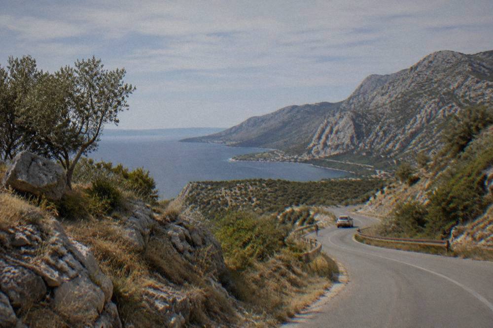 A road winding through dry karst hills toward the coast on a clear summer day.