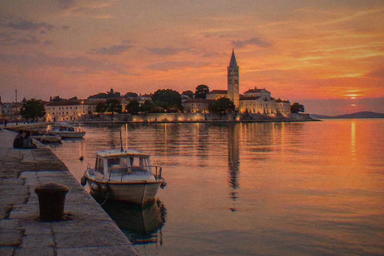Zadar Old Town peninsula seen across the harbour at dusk, reflected in still water.