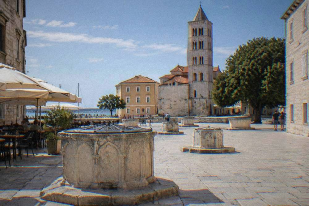 Five Wells Square in Zadar Old Town with its stone wells, cafe tables and a tower.