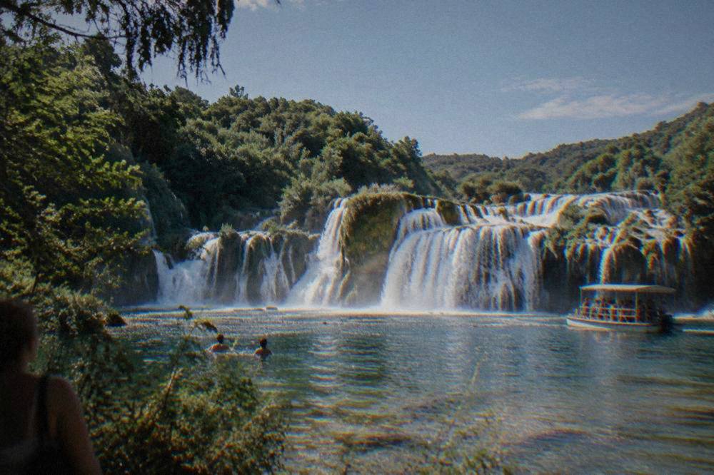A wide travertine waterfall spreading across a natural stone barrier in summer.
