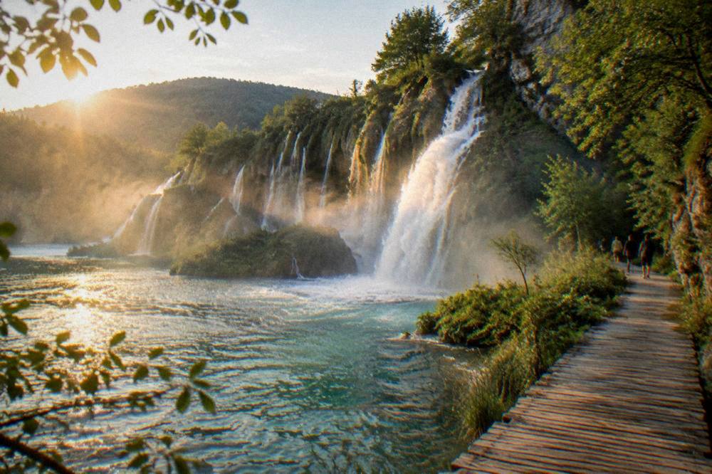 A few distant visitors on a wooden boardwalk beside a rushing waterfall.