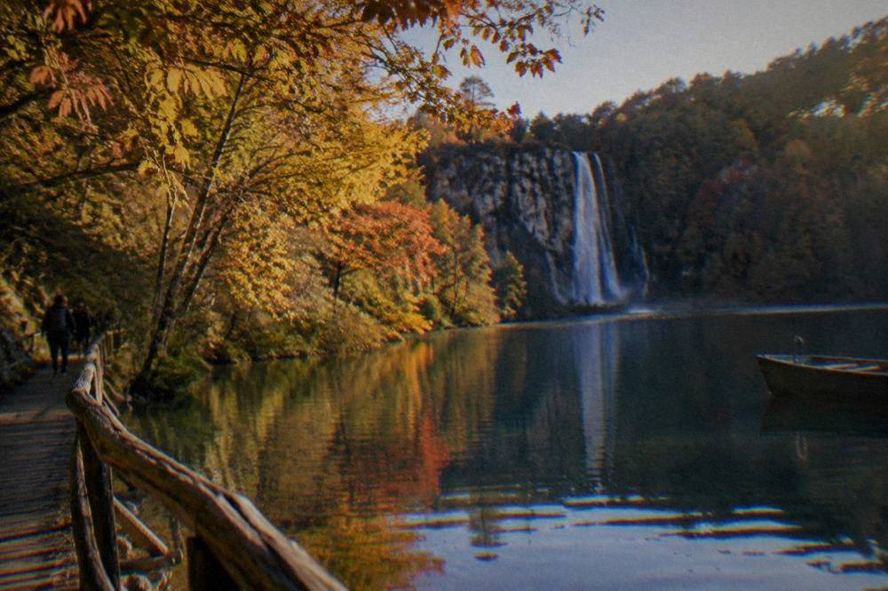 Autumn trees above a calm lake with a waterfall in the distance.