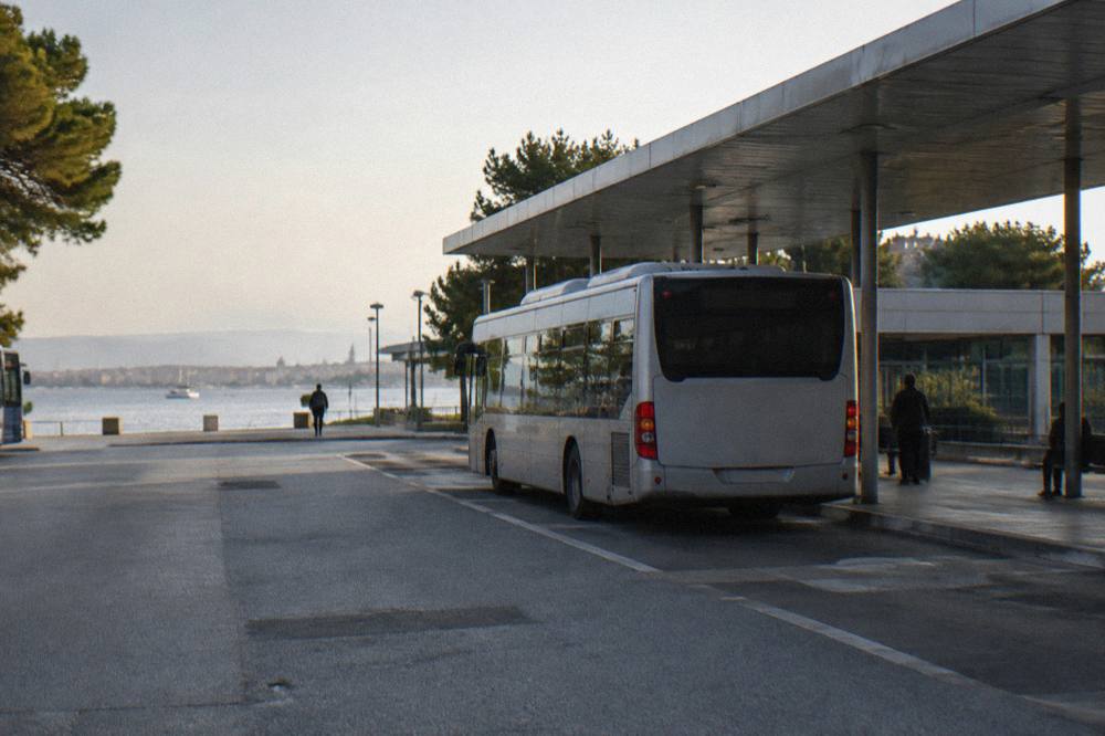 A city bus parked at a coach station with a sheltered bay and trees.