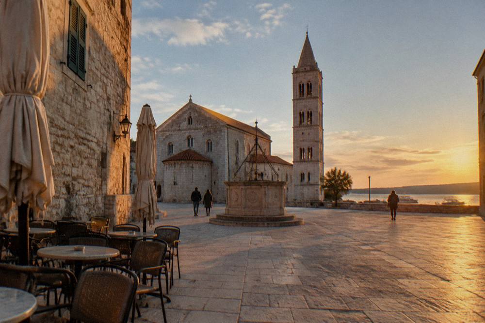 A pale stone Old Town square in soft autumn light with empty cafe chairs.