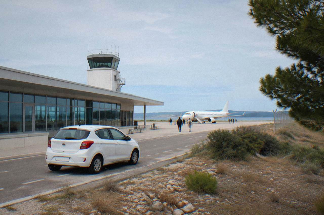A white car parked outside a small airport terminal under a clear sky.
