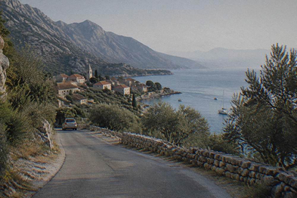 A coastal road winding past low stone walls toward a Dalmatian village by the sea.