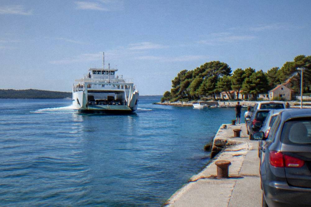 A ferry approaching a small island harbour with cars waiting on the quay.