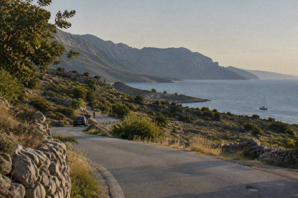 A road through low Dalmatian countryside of stone walls and scrub toward the coast.