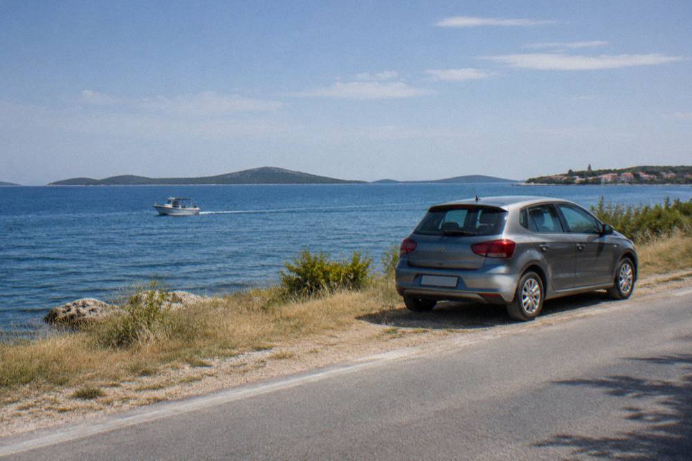 A parked car on a coastal road with islands visible across the blue water.