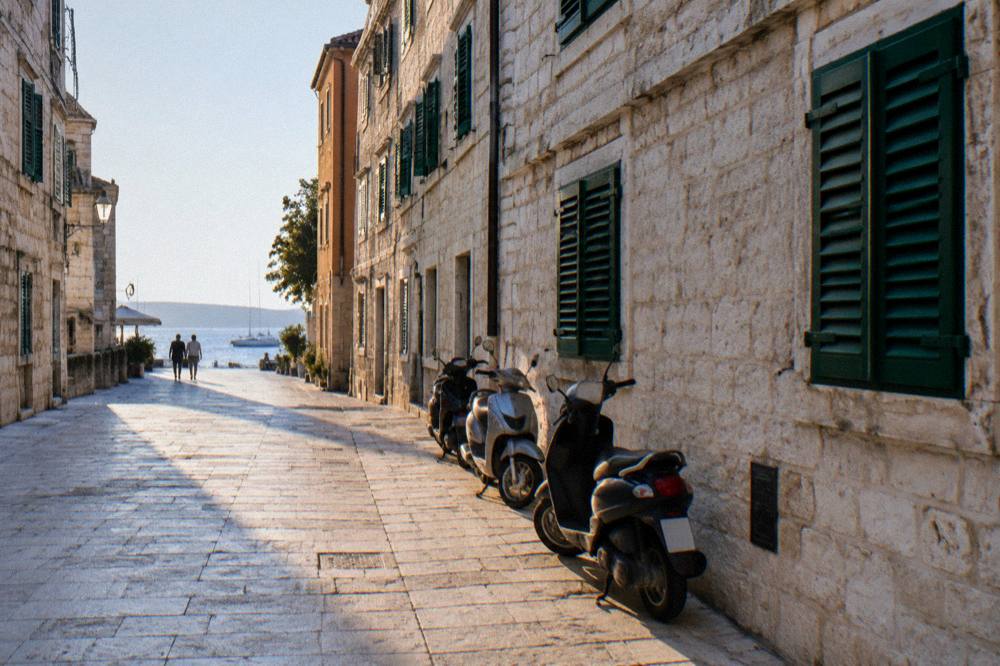 A pale stone street in Zadar old town with parked scooters against the wall.