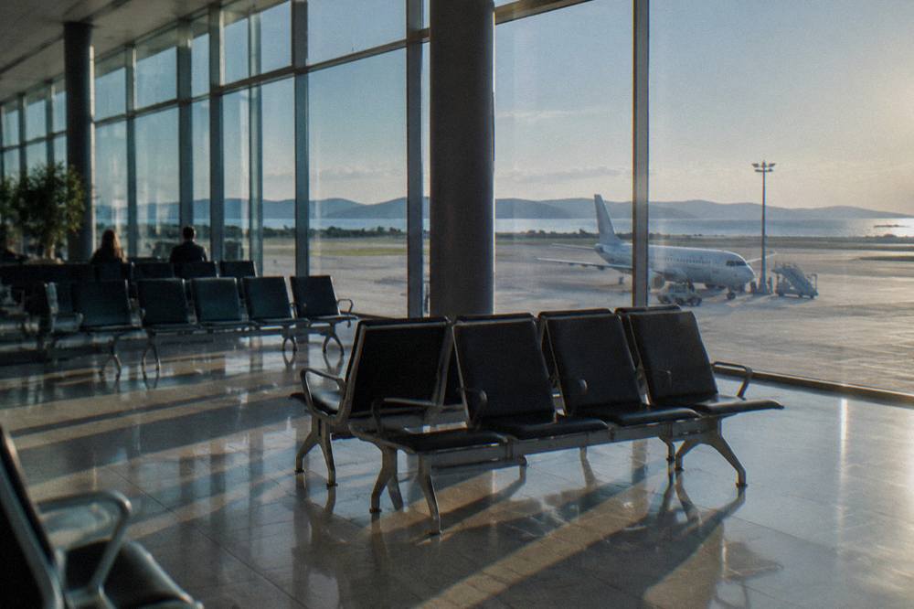 A bright modern airport hall with tall glass walls and rows of empty seats.