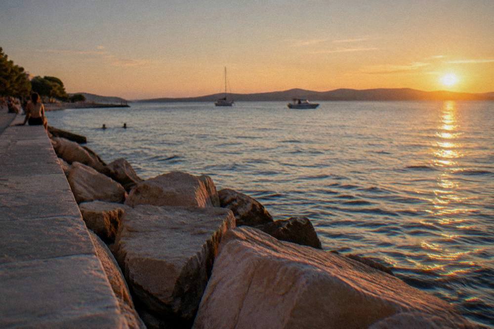Sunlight over a calm Adriatic with a low island coastline and a stone breakwater.