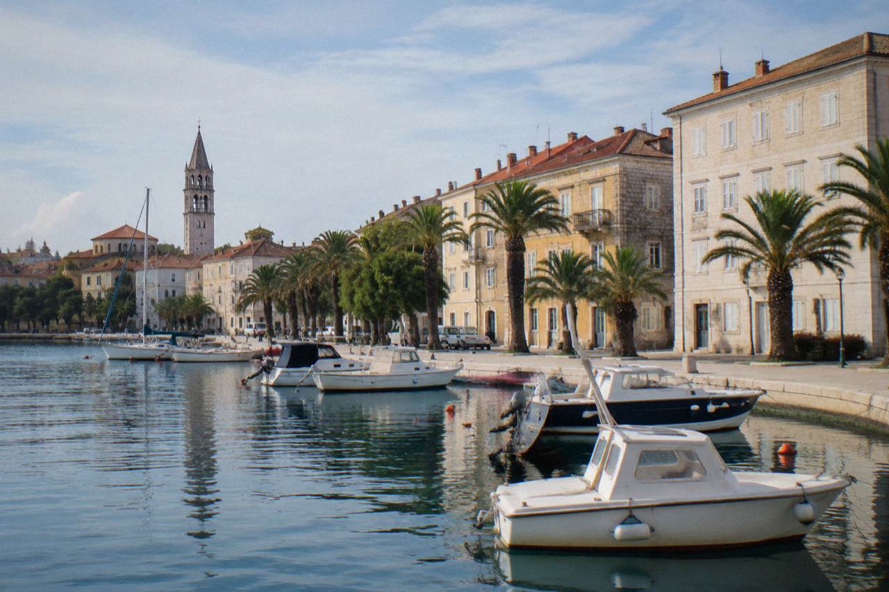 Apartment buildings along Zadar's seafront with moored boats on calm morning water.
